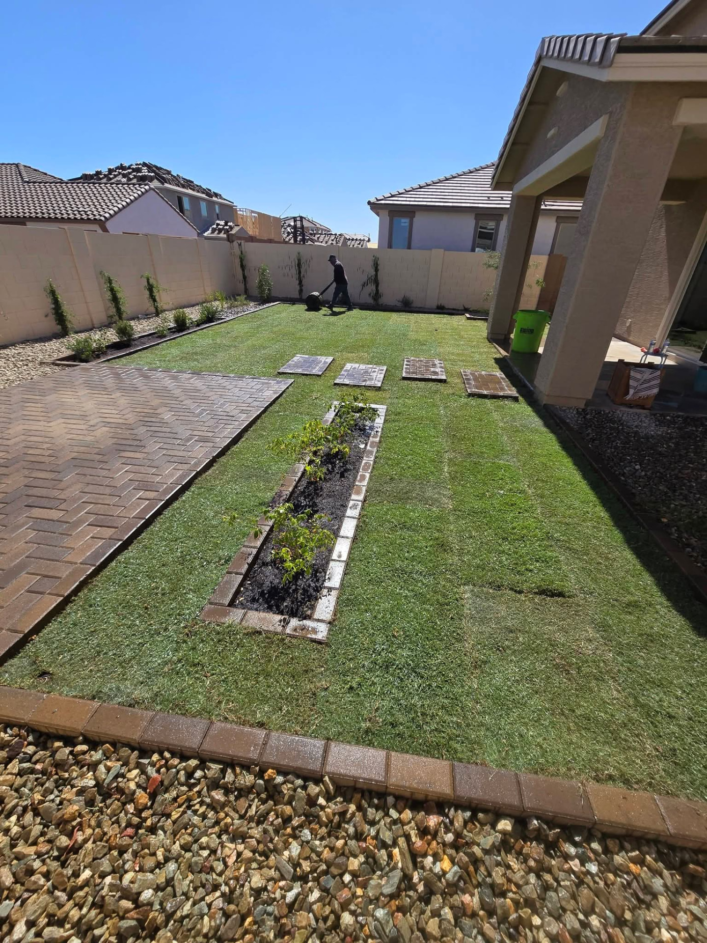 The same backyard finished with a full green lawn, filled planting beds, and completed paver walkway