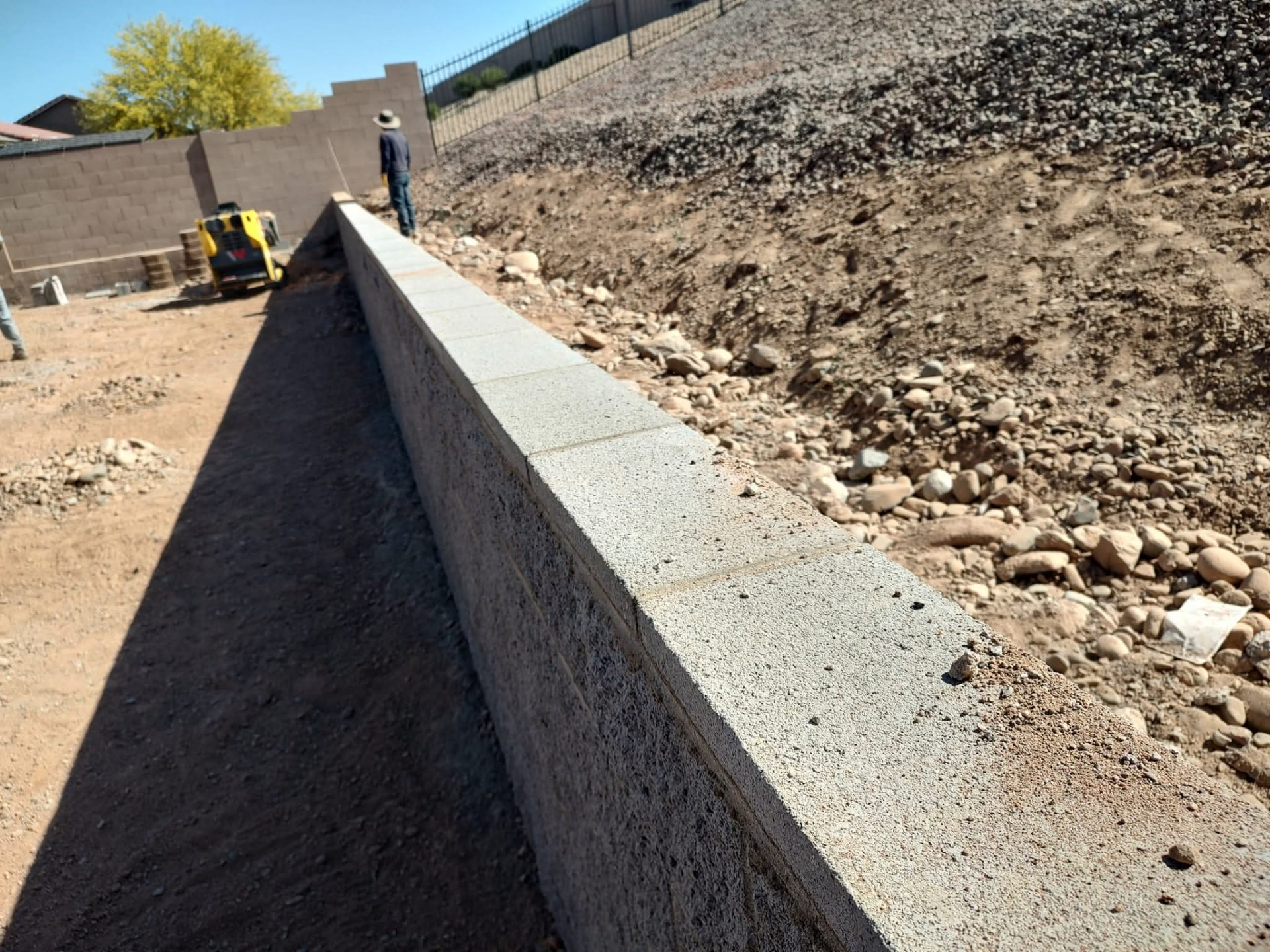 Completed block retaining wall holding back the graded hillside along the property line